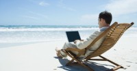 Businessman Sitting in Lounge Chair on Beach, Barefoot, Using Laptop